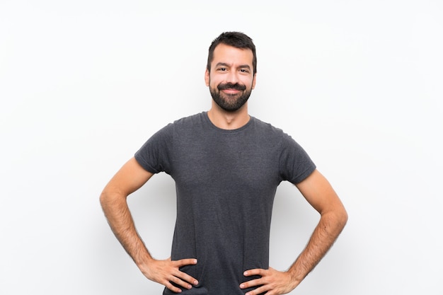 Joven guapo sobre pared blanca aislada posando con los brazos en la cadera y sonriendo