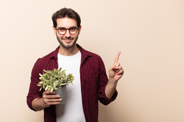 Joven guapo sonriendo alegremente, sintiéndose feliz y apuntando hacia un lado y hacia arriba, mostrando el objeto en el espacio de la copia