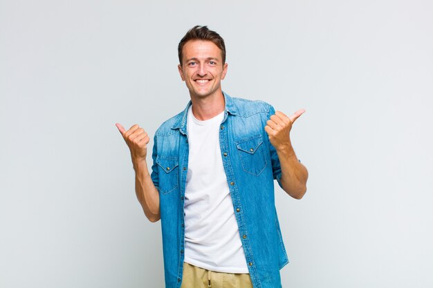 Joven guapo sonriendo con alegría y luciendo feliz, sintiéndose despreocupado y positivo con ambos pulgares hacia arriba