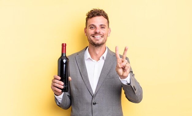 joven guapo sonriendo y luciendo amigable, mostrando el número dos. concepto de botella de vino