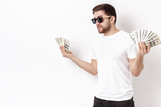 Joven guapo sonriente con barba en una camisa blanca sosteniendo un montón de billetes de cien dólares. dinero