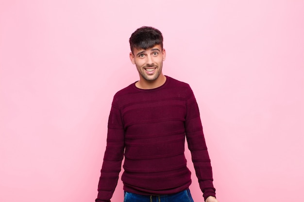 Joven guapo con una sonrisa grande, amigable y despreocupada, con aspecto positivo, relajado y feliz, escalofriante contra la pared rosa