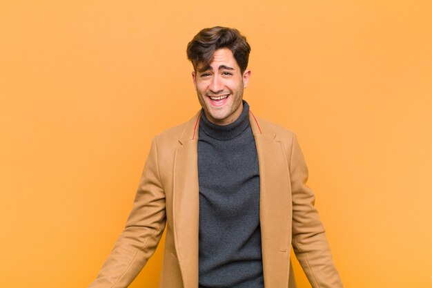 Joven guapo con una sonrisa grande, amigable y despreocupada, se ve positivo, relajado y feliz, escalofriante contra el fondo naranja