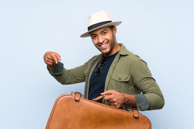 Joven guapo sosteniendo un maletín vintage sobre pared azul aislado y apuntando