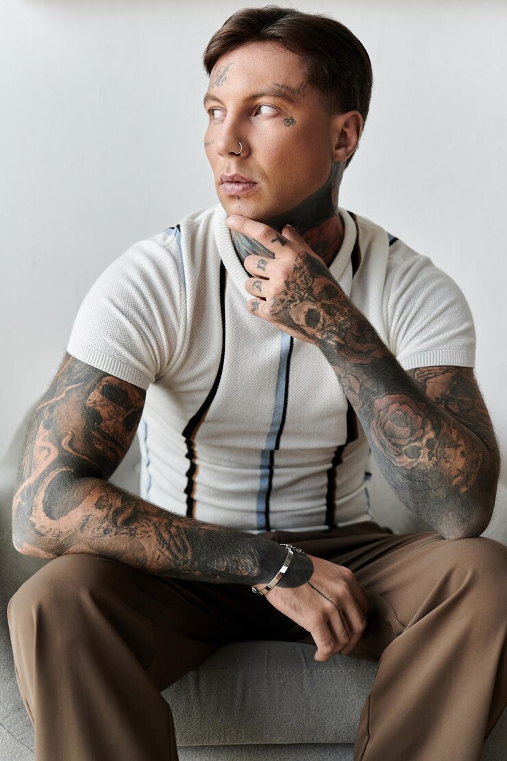 Un joven guapo con tatuajes se sienta casualmente contemplando mientras está vestido con estilo