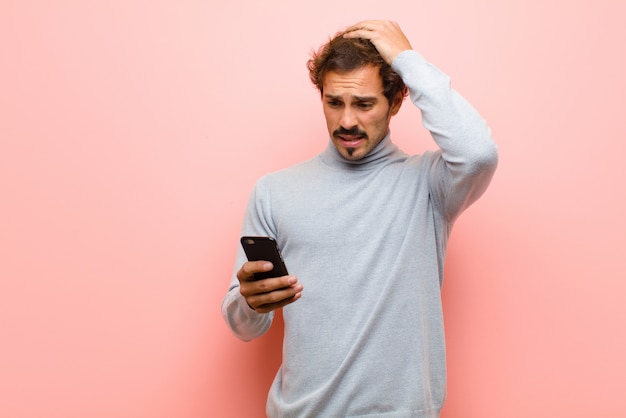 Joven guapo con un teléfono inteligente contra la pared plana rosa