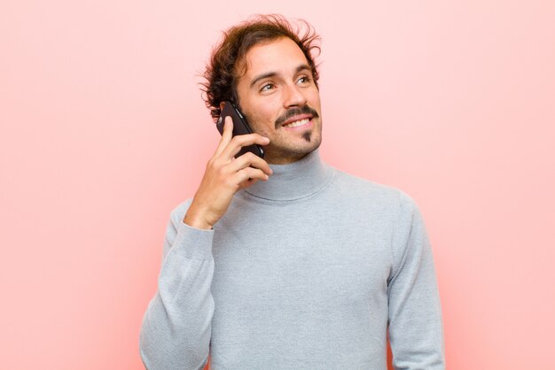 Joven guapo con un teléfono inteligente contra la pared plana rosa