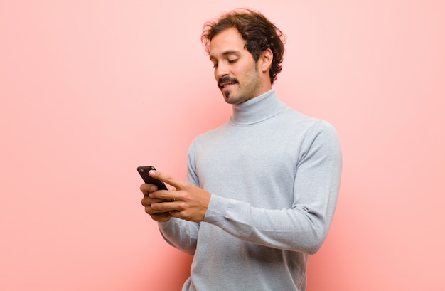 Joven guapo con un teléfono inteligente en pared plana rosa