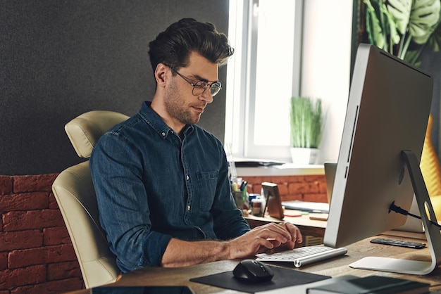 Un joven guapo usando una computadora mientras está sentado en su lugar de trabajo en la oficina