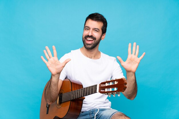 Joven con guitarra sobre azul aislado contando diez con los dedos