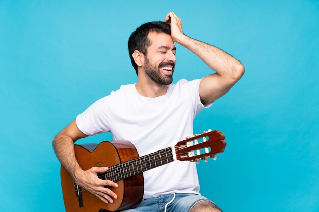 Joven con guitarra sobre azul aislado se ha dado cuenta de algo y tiene la intención de la solución