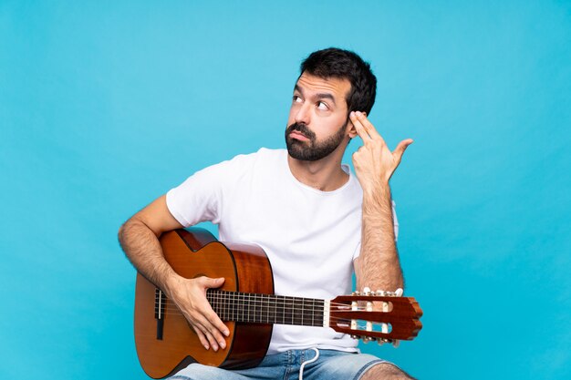 Joven con guitarra sobre azul aislado con problemas para hacer el gesto de suicidio