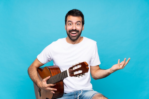 Joven con guitarra sobre azul con expresión facial sorprendida