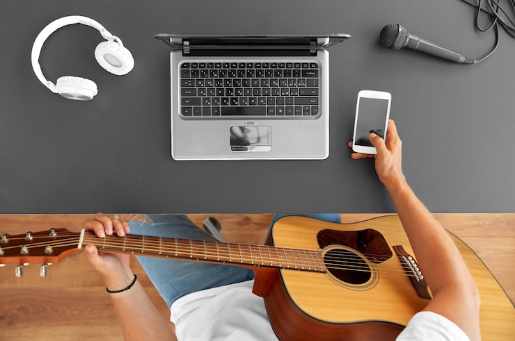 Foto joven con guitarra y teléfono inteligente en la mesa
