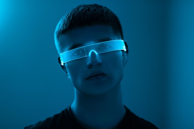 Joven en una habitación de neón azul con gafas cibernéticas, foto de alta calidad