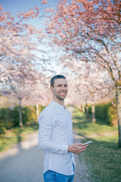 Un joven habla por teléfono de un floreciente jardín de sakura. Primavera.