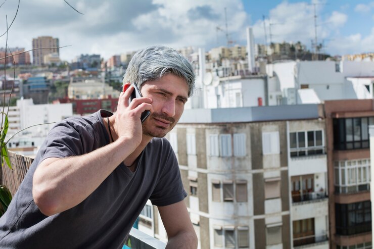 Joven hablando por su teléfono inteligente apoyado en la terraza