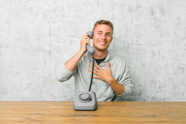 Joven hablando por un teléfono antiguo se ríe a carcajadas manteniendo la mano en el pecho.