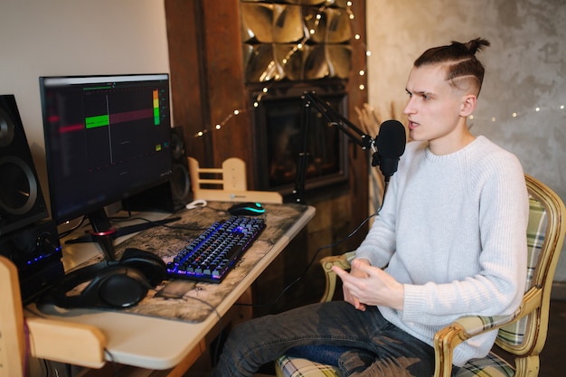 Foto joven hace una grabación de audio de podcast en casa hombre usando pc y dos micrófonos profesionales