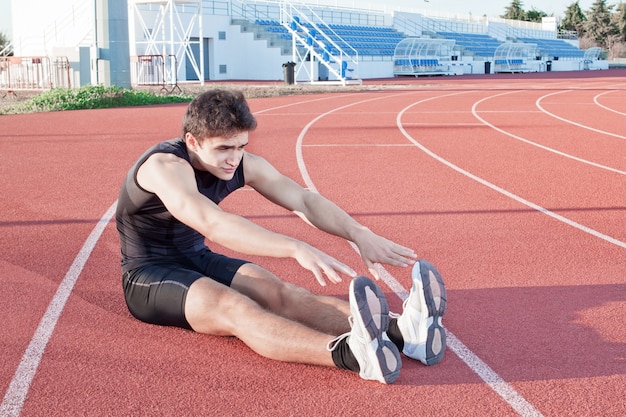 Un joven hace que un atleta se estire. Contra el fondo del estadio.