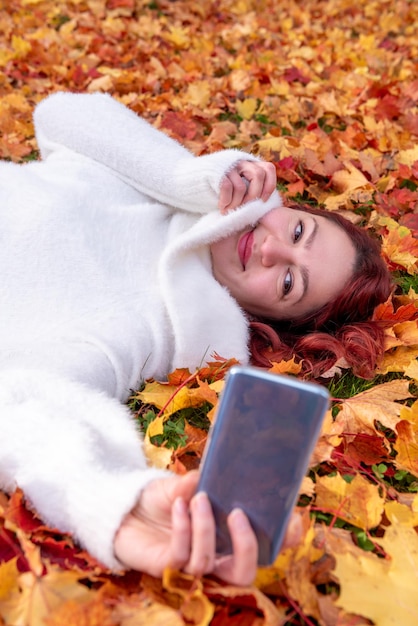 Una joven se hace una selfie mientras está sentada en el suelo rodeada de hojas de otoño