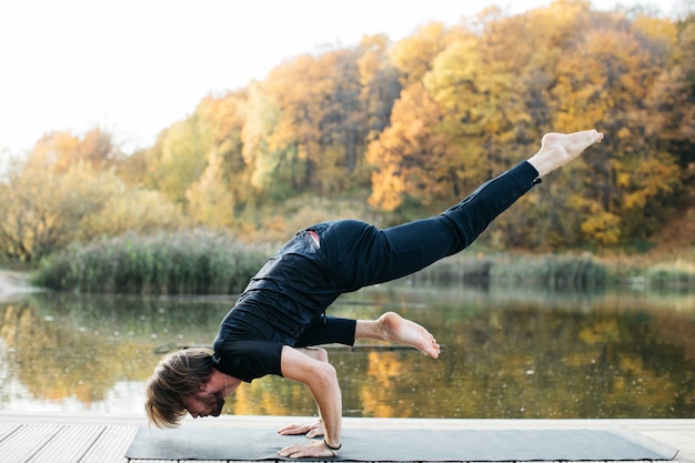 Joven haciendo asanas de yoga en la naturaleza cerca del lago