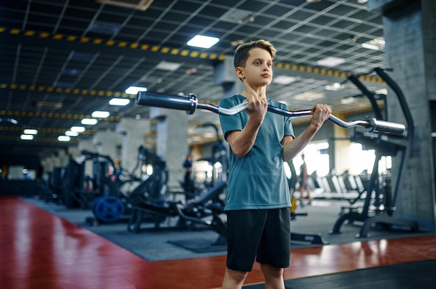 Joven haciendo ejercicio con barra en el gimnasio. Niño en entrenamiento físico en club deportivo, salud y estilo de vida saludable, colegial en entrenamiento, juventud deportiva