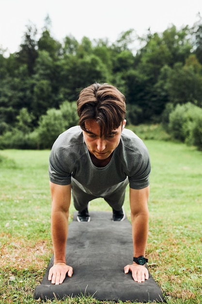 Foto joven haciendo flexiones afuera en la hierba durante su entrenamiento de calistenia