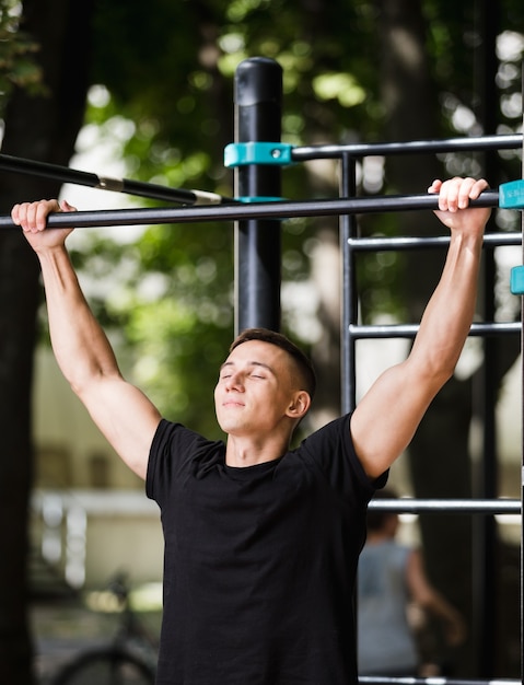 Joven haciendo flexiones en la barra horizontal al aire libre, entrenamiento, concepto de deporte.