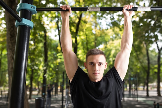 Joven haciendo flexiones en la barra horizontal al aire libre, entrenamiento, concepto de deporte.