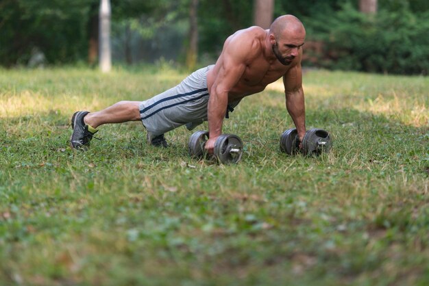 Joven haciendo flexiones con pesas al aire libre