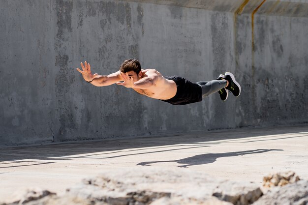 Joven haciendo flexiones con salto sin camisa en la calle