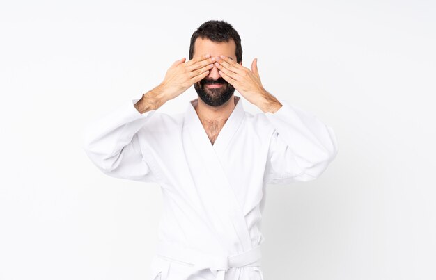 Joven haciendo karate sobre blanco cubriendo los ojos con las manos