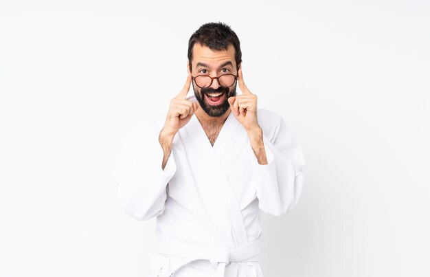 Joven haciendo karate sobre blanco con gafas y sorprendido