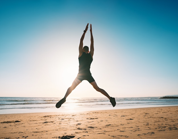 Joven haciendo saltos de tijera o ejercicio de salto de estrellas en la playa por la mañana