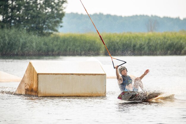 Foto joven haciendo wakeboard en un lago haciendo raley frontroll y saltando los kickers y sliders wakeboard