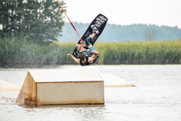 Foto joven haciendo wakeboard en un lago haciendo raley frontroll y saltando los kickers y sliders wakeboard