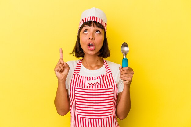 Joven heladero de raza mixta mujer sosteniendo una bola de helado aislado sobre fondo amarillo