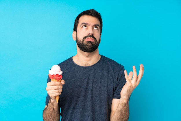 Joven con un helado de cucurucho sobre pared azul aislado frustrado por una mala situación