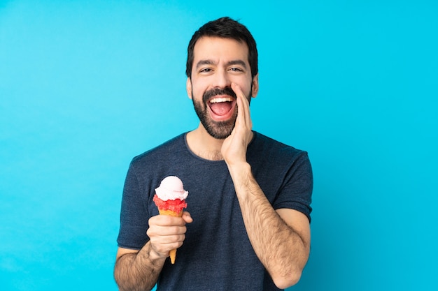 Joven con un helado de cucurucho sobre pared azul aislado gritando con la boca abierta