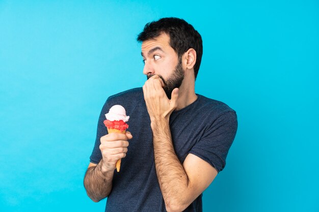 Joven con un helado de cucurucho sobre pared azul aislado nervioso y asustado poniendo las manos en la boca