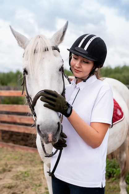 Joven hembra activa abrazos hocico de caballo de carreras de pura raza blanca o yegua durante el frío en el entorno rural