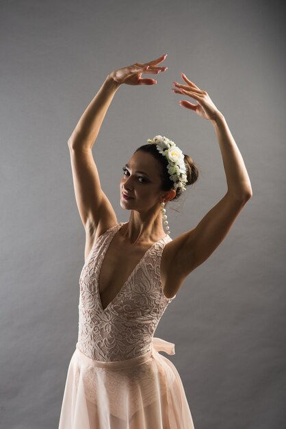 Joven hermosa bailarina de ballet en traje de baño beige posando en pointes sobre fondo gris claro de estudio