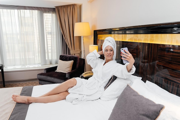 Foto una joven hermosa con una bata blanca está hablando por teléfono en su habitación de hotel descanso y viajes recreación y turismo del hotel
