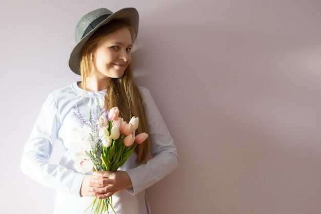 Una joven hermosa con cabello largo rubio disuelto y un sombrero de fieltro en la cabeza mantiene flores de primavera