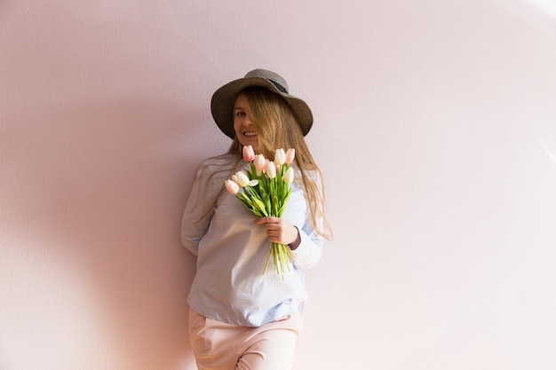 Una joven hermosa con cabello largo rubio disuelto y un sombrero de fieltro en la cabeza mantiene flores de primavera