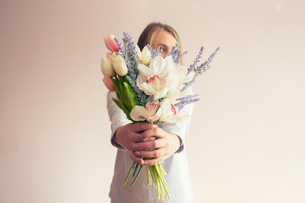 Una joven hermosa con cabello largo rubio disuelto y un sombrero de fieltro en la cabeza mantiene flores de primavera