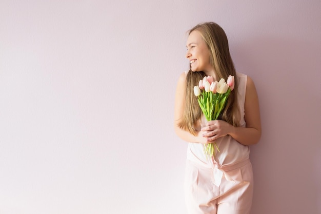 Una joven hermosa con cabello largo rubio disuelto y un sombrero de fieltro en la cabeza mantiene flores de primavera