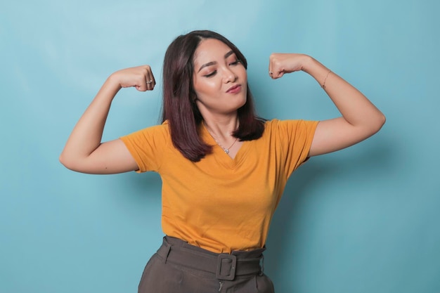 Una joven hermosa con una camiseta amarilla casual parada sobre un fondo azul aislado mostrando los músculos de los brazos sonriendo orgulloso Concepto de fitness