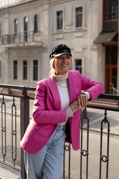 Una joven hermosa con una chaqueta larga de color rosa y un sombrero negro camina por la calle